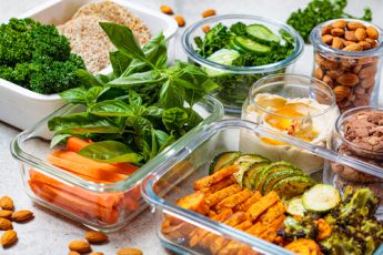 meals prepped into separate containers along with a jar contains almonds and another contained chocolate cookies