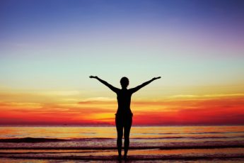 Person with arms in the air in front of a scenic sunset by the sea