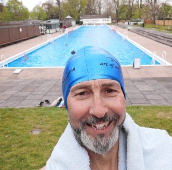 man smiling in a swimming cap pictured in front of a swimming pool