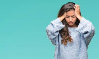 woman in blue jumper holding her head with a pained expression
