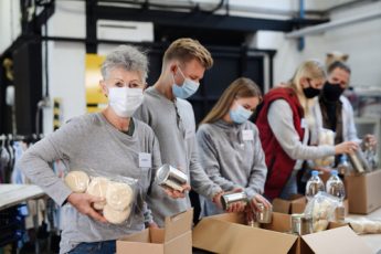 People in face masks packing boxes with cans, water bottles and bread.